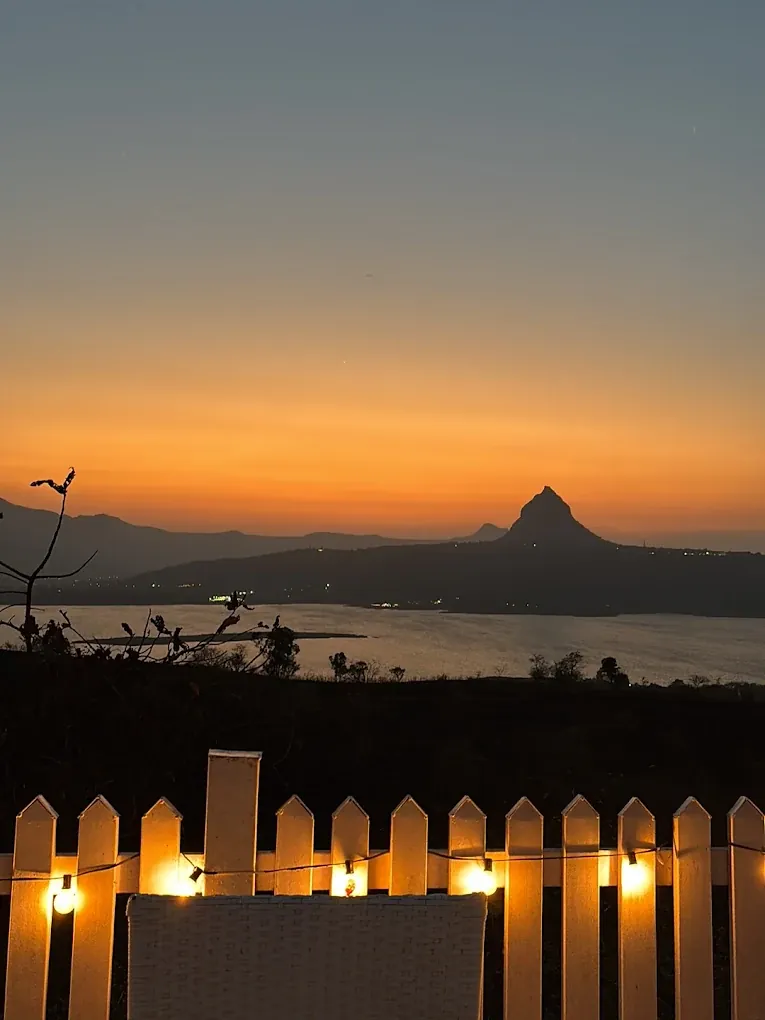 Open-air deck lit with fairy lights at sunset overlooking Pawna Lake