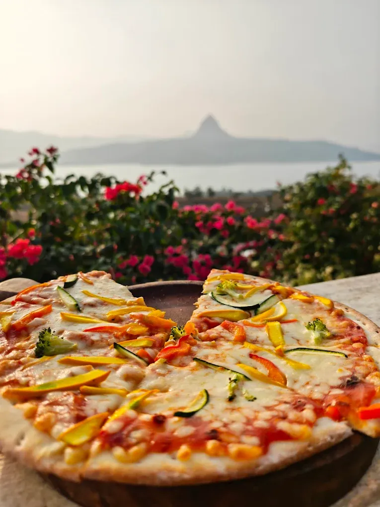 Veg pizza plated beside flowers with a Pawna Lake view
