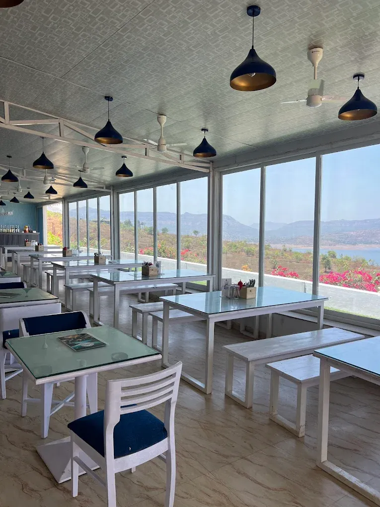 Indoor dining beside large windows framing the Pawna Lake view